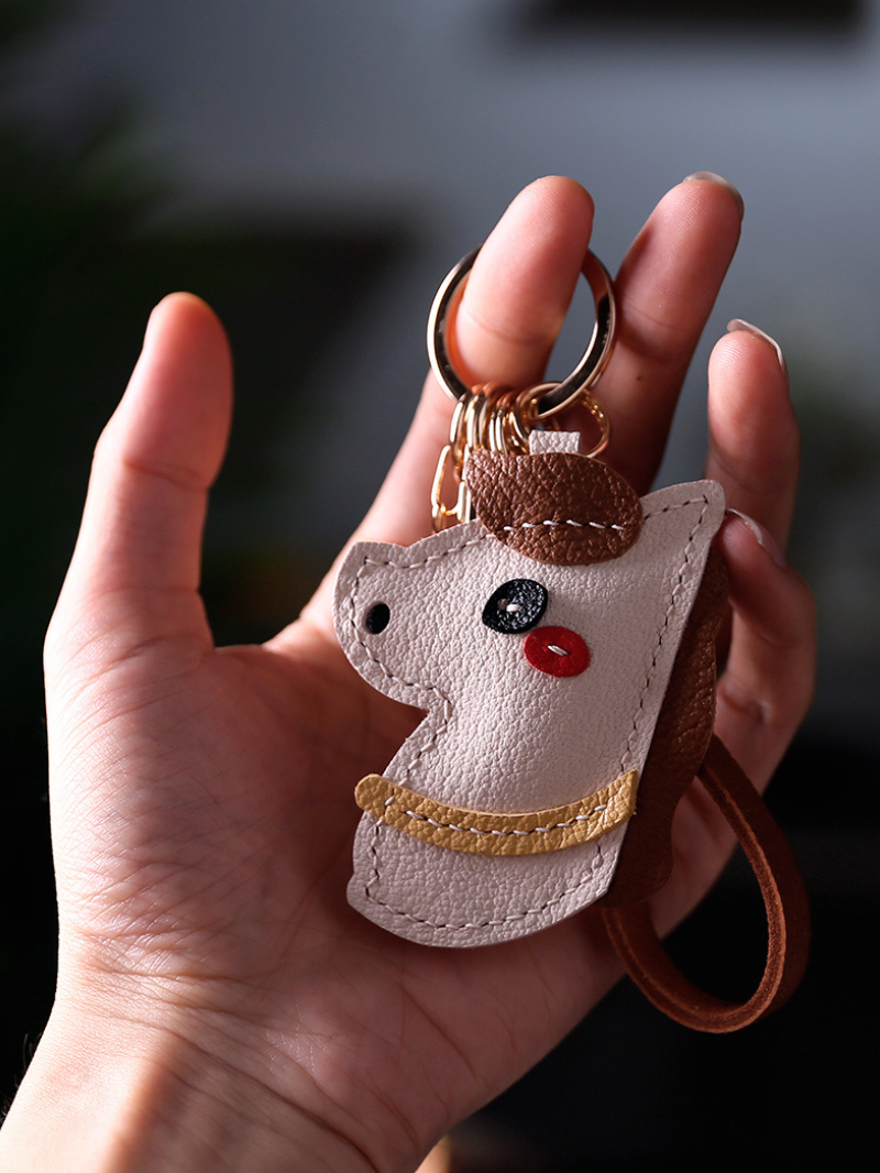 Hand holding a white cat-shaped keychain with a gold collar against a dark background